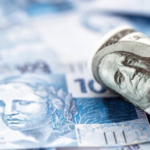 100 US dollar banknote over many Brazilian hundred dollar bills, a concept of high dollar against the Brazilian currency