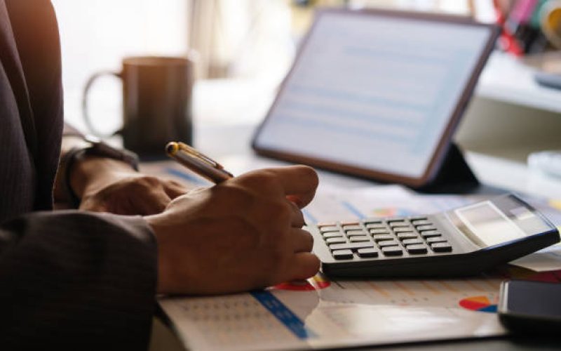 Millennial businessman working with digital tablet, using calculator to check the statistics and projections.