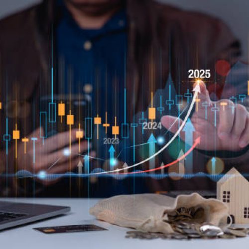 A man is sitting at a desk with a laptop and a bag of coins. He is looking at a graph on the laptop screen
